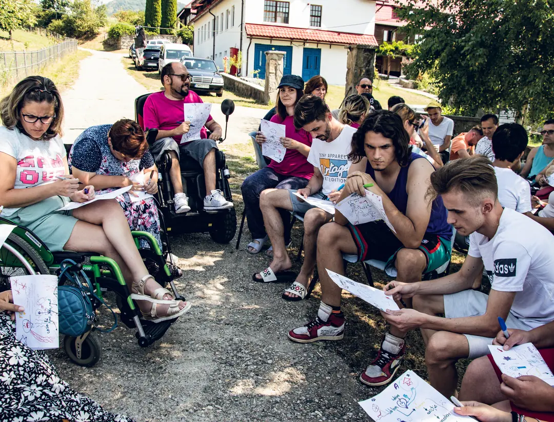 Participanți care scriu și desenează, așezați în cerc