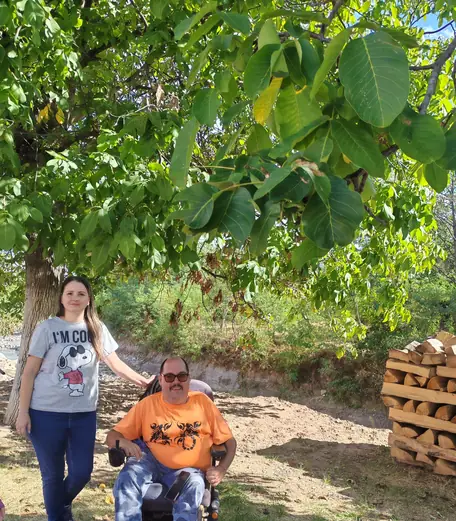 Un bărbat în scaun rulant și o femeie, sub un nuc