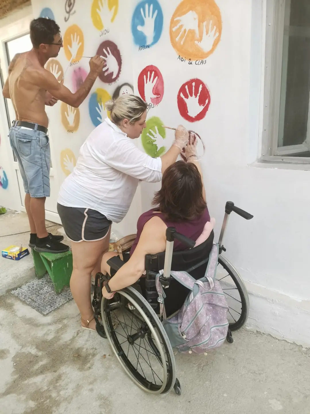 Trei oameni pictează amprente colorate pe perete