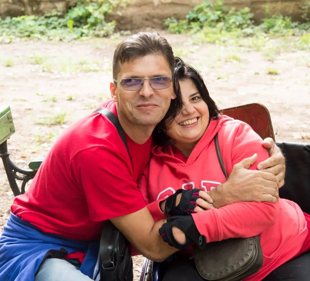 Un bărbat și o femeie în scaun rulant, îmbrățișați și zâmbind
