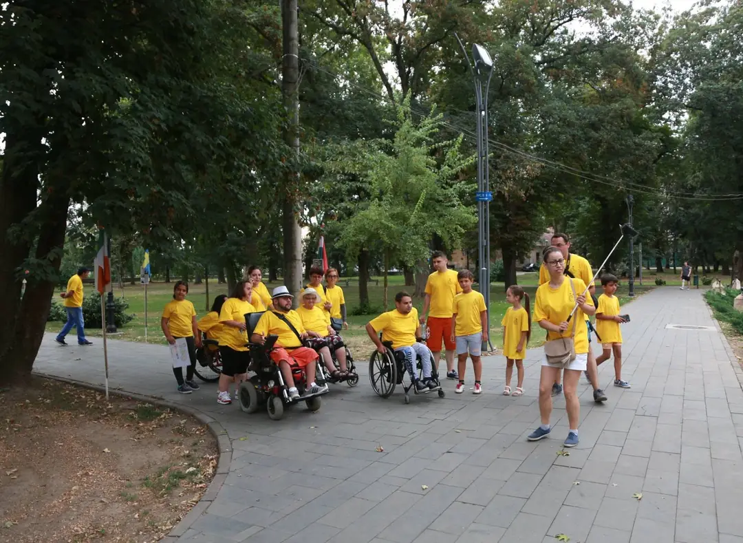 Volunteers in yellow T-shirts walking through a park with participants in wheelchairs