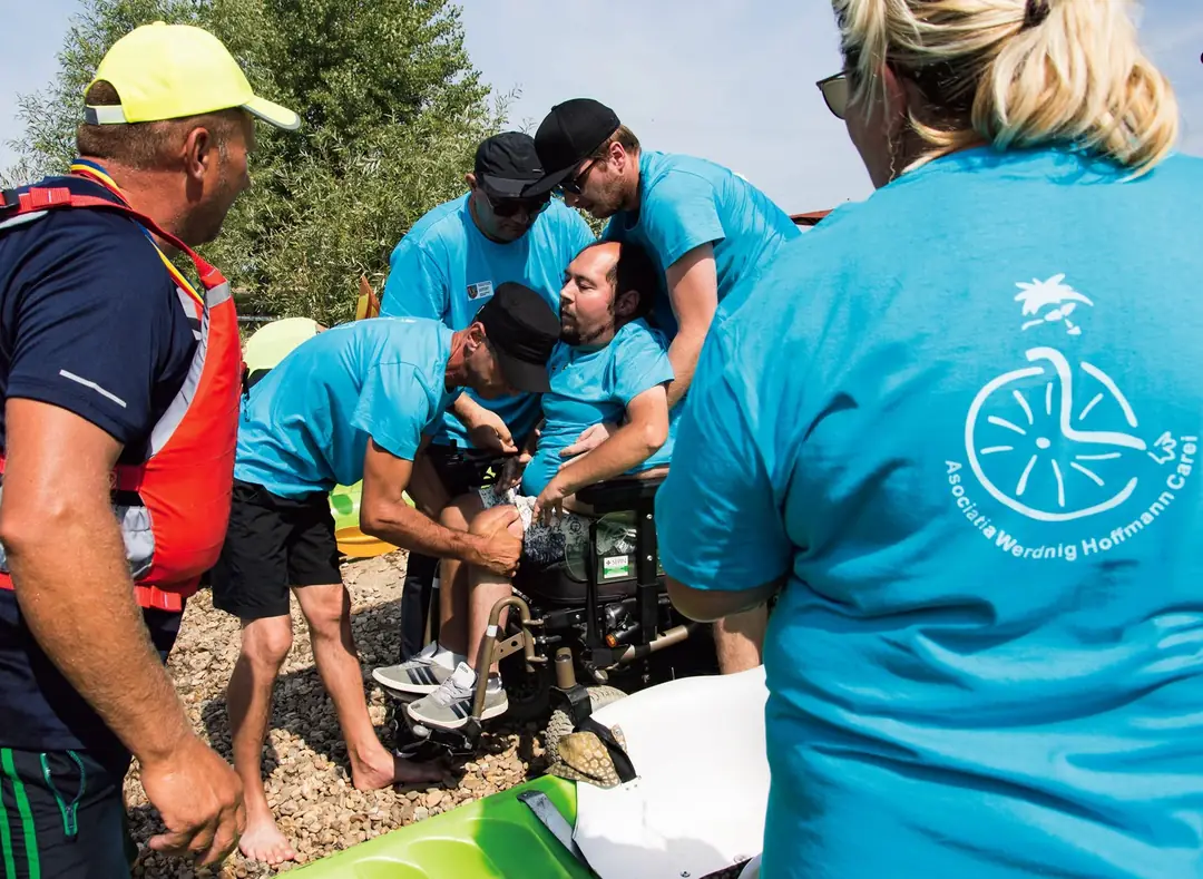 Voluntari ajută un participant în scaun rulant să urce în caiac